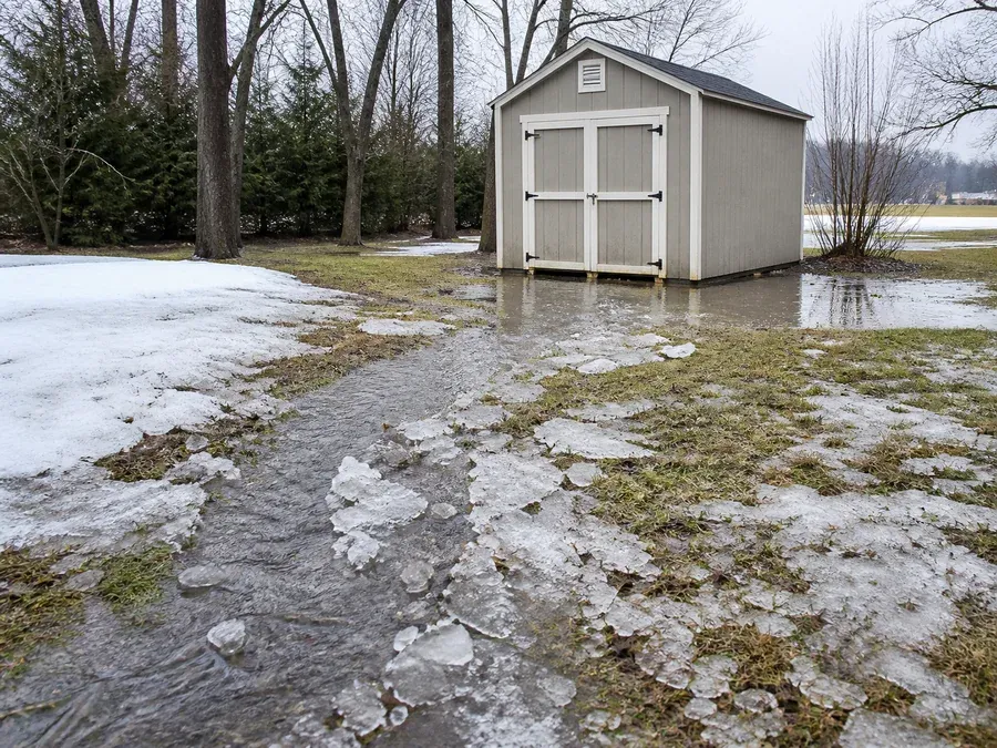 Rapid ice-melt runoff crossing normally dry ground and reaching a detached shed